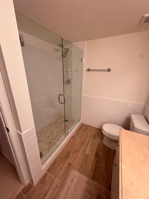 full bath with toilet, wood tiled floor, visible vents, wainscoting, and a shower stall