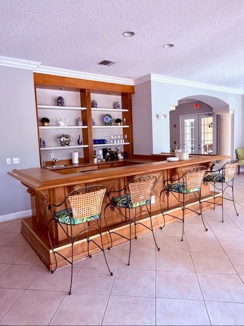 bar featuring a textured ceiling, visible vents, crown molding, arched walkways, and a bar