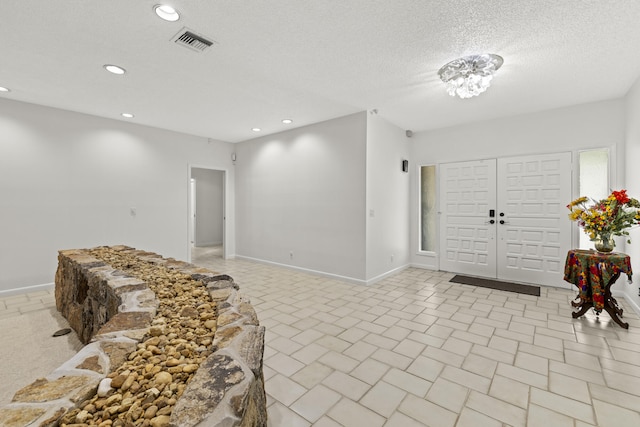 foyer entrance with a textured ceiling, visible vents, baseboards, and recessed lighting