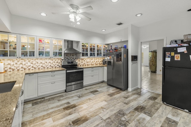 kitchen featuring ceiling fan, white cabinetry, backsplash, wall chimney range hood, and stainless steel appliances