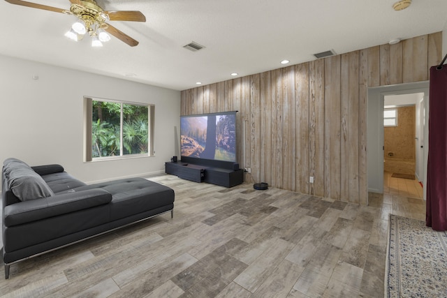 cinema room with wood finished floors, a ceiling fan, a wealth of natural light, visible vents, and wooden walls