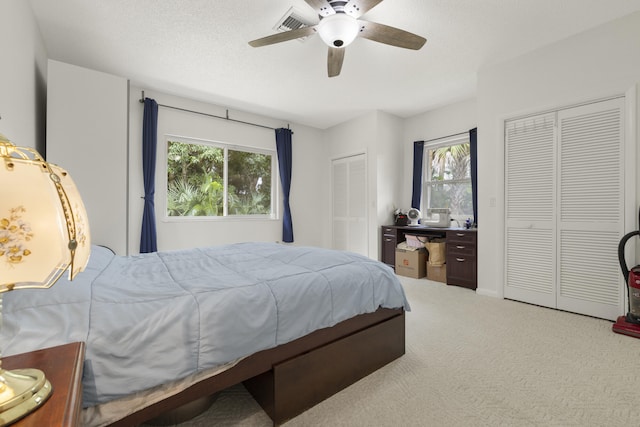 carpeted bedroom with two closets, a ceiling fan, visible vents, and multiple windows