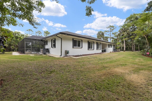 rear view of property with a yard, a patio, stucco siding, and glass enclosure