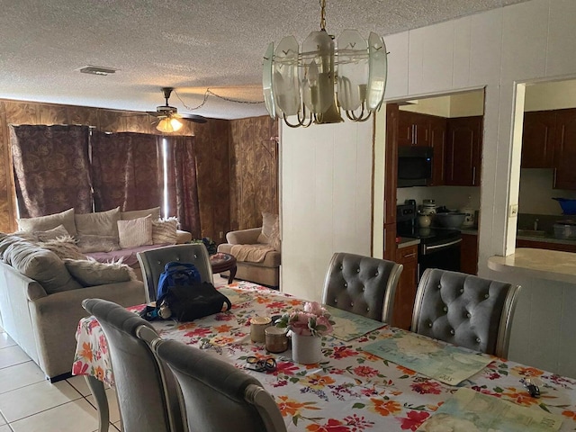 dining area featuring a textured ceiling, visible vents, wood walls, light tile patterned floors, and ceiling fan with notable chandelier