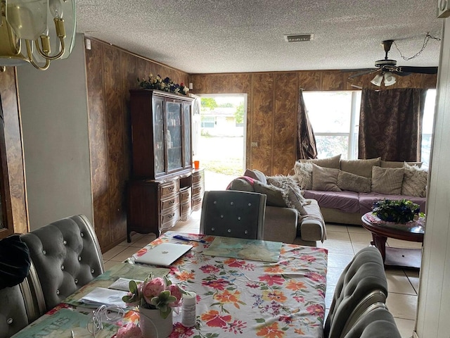 dining space with visible vents, ceiling fan, light tile patterned floors, and wooden walls