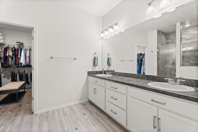 full bathroom featuring a sink, a shower stall, double vanity, wood finished floors, and a spacious closet