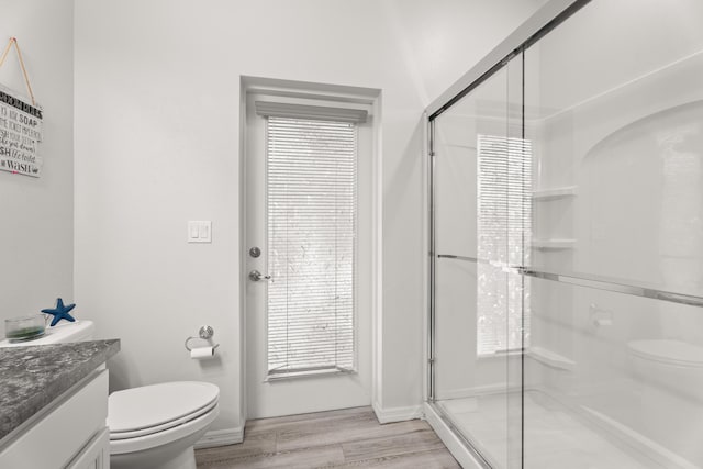 bathroom featuring toilet, wood finished floors, vanity, a stall shower, and baseboards