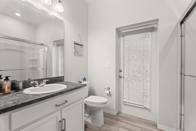 bathroom featuring toilet, a shower with door, wood finished floors, and vanity