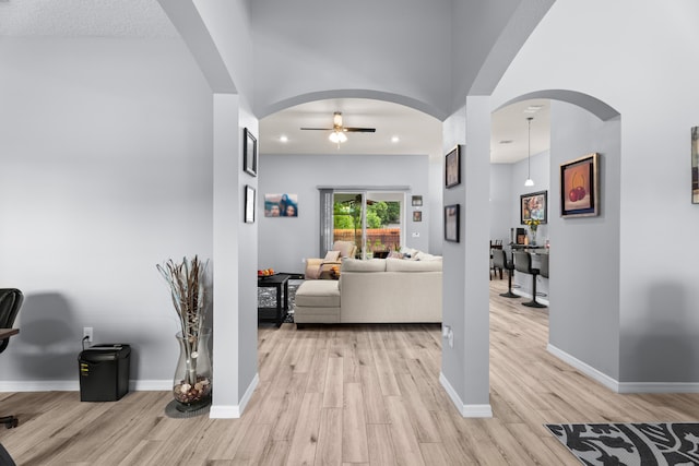 corridor with light wood finished floors, arched walkways, baseboards, and recessed lighting