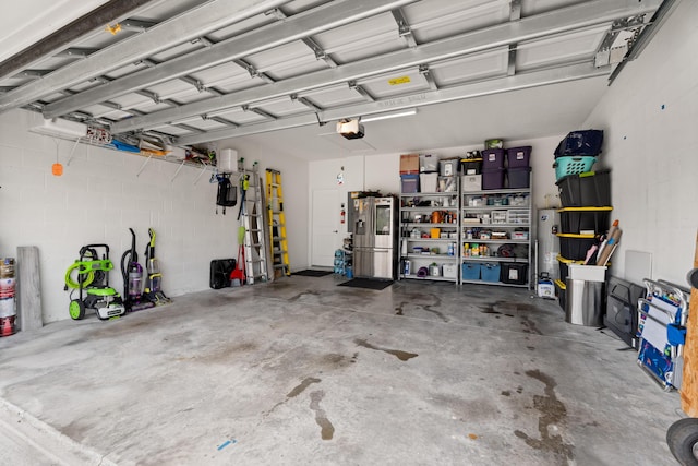 garage featuring stainless steel fridge, concrete block wall, and a garage door opener