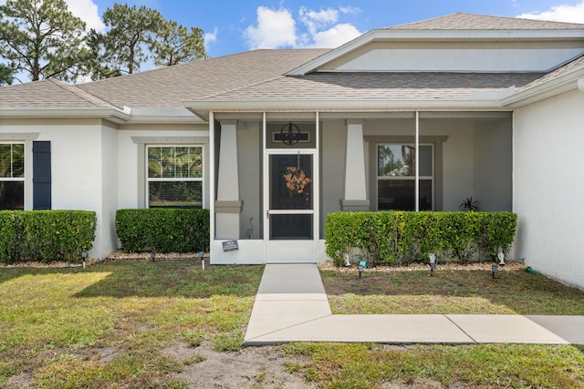 entrance to property with a lawn, stucco siding, and roof with shingles