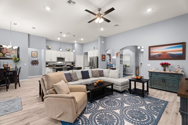 living room with light wood-type flooring, visible vents, ceiling fan with notable chandelier, and arched walkways