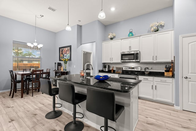 kitchen with a kitchen island with sink, stainless steel appliances, tasteful backsplash, light wood-type flooring, and a high ceiling