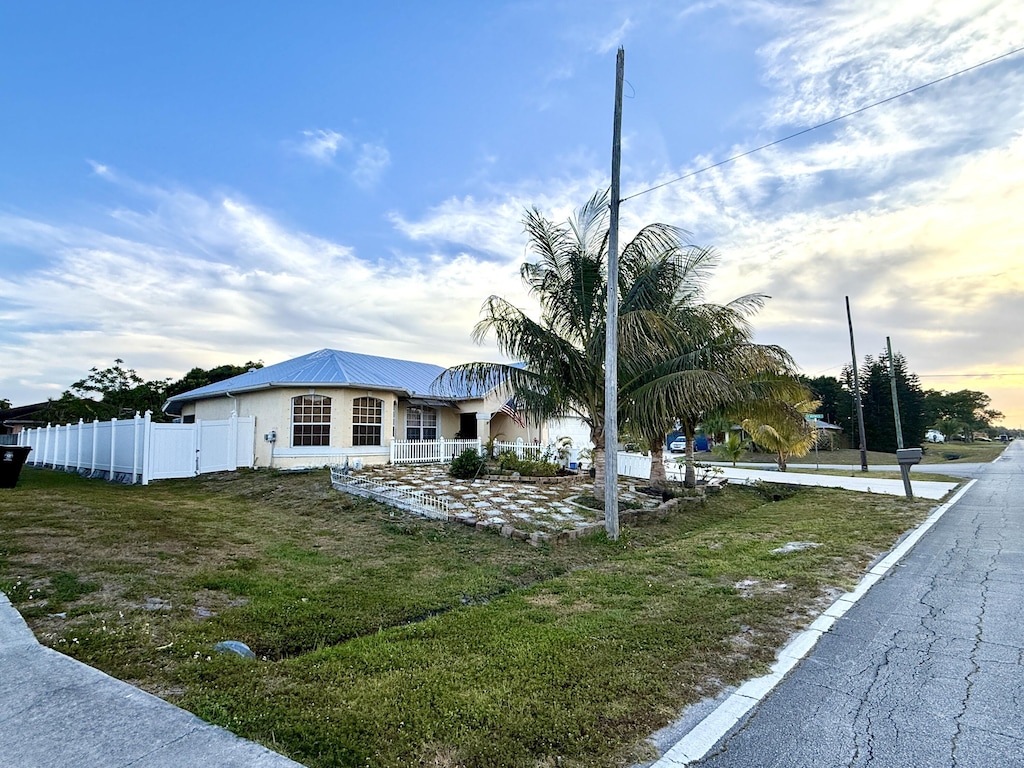 view of front of property featuring metal roof, stucco siding, a front lawn, and fence