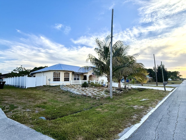 view of front of property featuring metal roof, stucco siding, a front lawn, and fence