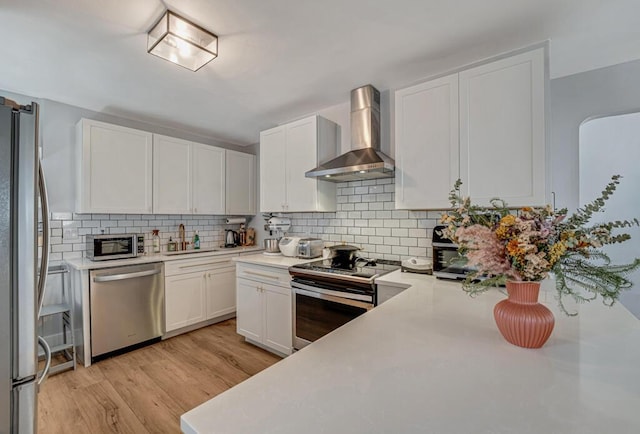 923 N H St, Lake Worth Beach, FL 33460 - kitchen with tasteful backsplash, light countertops, white cabinets, stainless steel appliances, and wall chimney exhaust hood