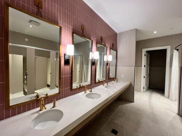 full bath with double vanity, a sink, and tile walls