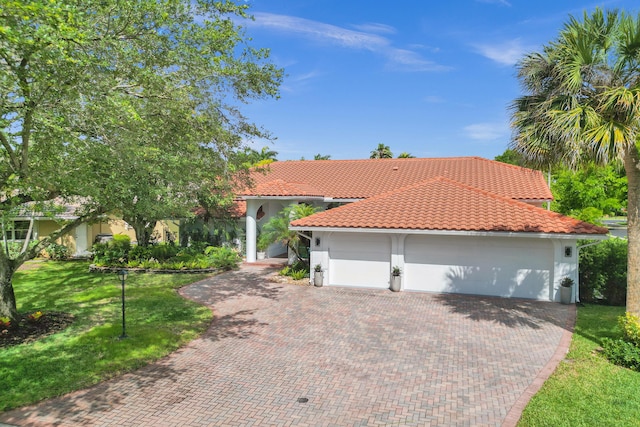 mediterranean / spanish-style home with decorative driveway, a tiled roof, stucco siding, an attached garage, and a front yard