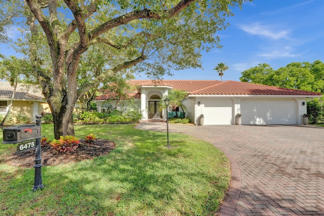 mediterranean / spanish-style home featuring a tile roof, decorative driveway, an attached garage, stucco siding, and a front yard
