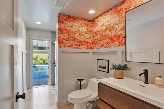 bathroom with toilet, vanity, recessed lighting, and a decorative wall