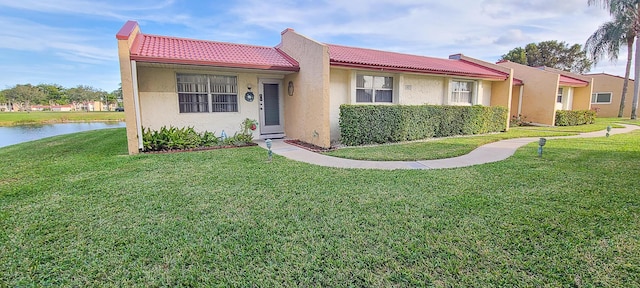 ranch-style house featuring a water view, a tiled roof, stucco siding, and a front yard