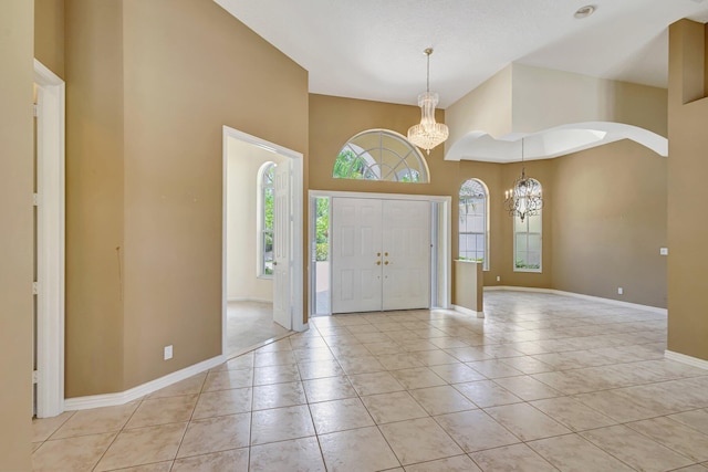 entryway with a chandelier, a high ceiling, baseboards, light tile patterned floors, and arched walkways