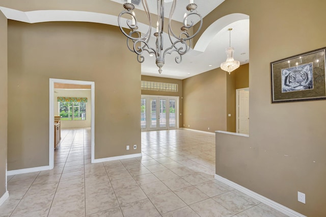 unfurnished room featuring a towering ceiling, a chandelier, plenty of natural light, light tile patterned floors, and arched walkways