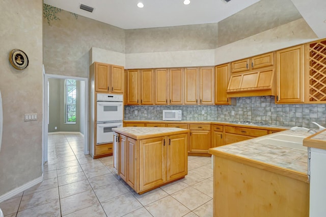 kitchen featuring white appliances, tile countertops, a kitchen island, backsplash, and a towering ceiling