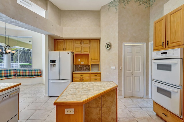 kitchen with white appliances, tile countertops, light tile patterned flooring, a high ceiling, and a chandelier