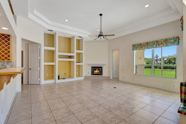 unfurnished living room featuring a raised ceiling, built in features, light tile patterned floors, a glass covered fireplace, and recessed lighting