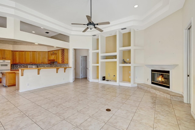 unfurnished living room featuring recessed lighting, light tile patterned floors, a tray ceiling, a ceiling fan, and built in features