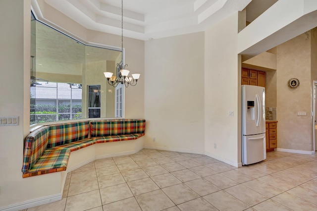 unfurnished dining area featuring light tile patterned flooring, a chandelier, baseboards, a towering ceiling, and a tray ceiling