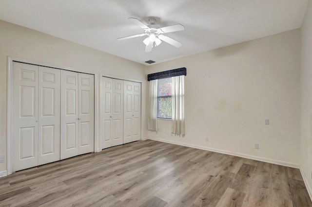unfurnished bedroom with multiple closets, light wood-style flooring, baseboards, and ceiling fan