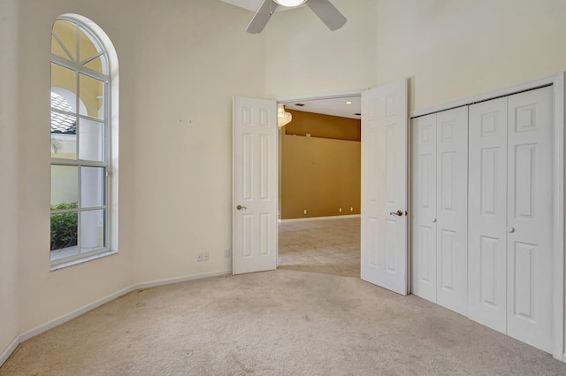unfurnished bedroom with light colored carpet, a towering ceiling, baseboards, a closet, and ceiling fan