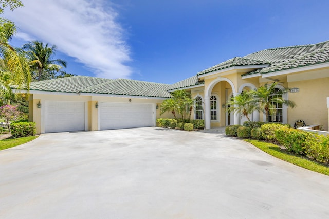 mediterranean / spanish-style home with stucco siding, driveway, a tiled roof, and an attached garage