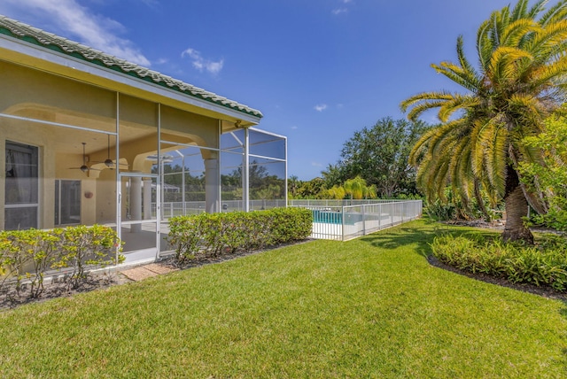 view of green lawn featuring a ceiling fan and glass enclosure