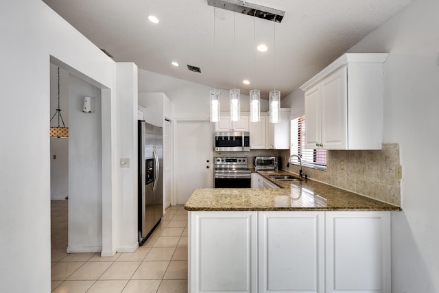 kitchen with appliances with stainless steel finishes, a peninsula, decorative backsplash, a sink, and dark stone counters