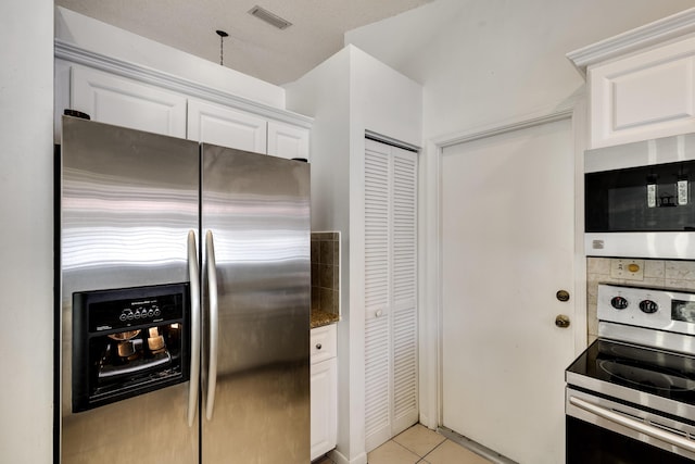 kitchen with appliances with stainless steel finishes, white cabinetry, light tile patterned floors, and dark stone counters