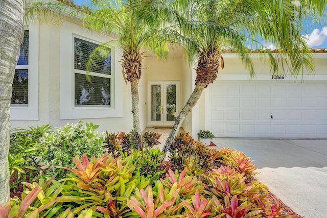 entrance to property featuring concrete driveway, stucco siding, french doors, and a garage