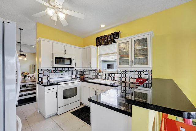 kitchen with a sink, a peninsula, white appliances, backsplash, and dark countertops