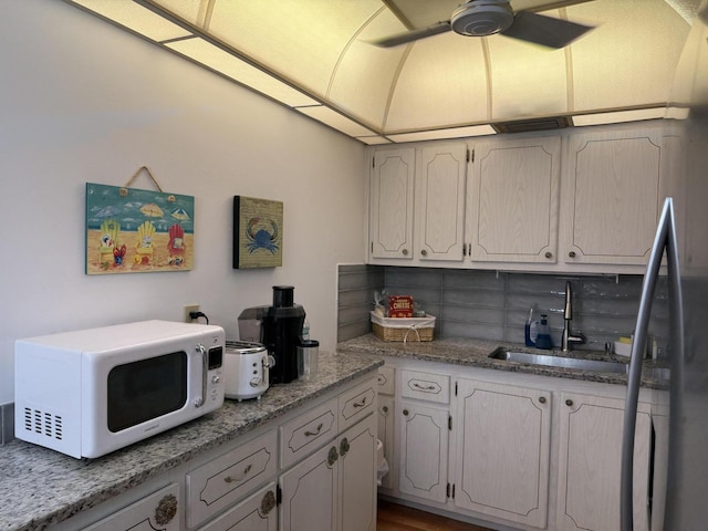 kitchen featuring a sink, white microwave, freestanding refrigerator, decorative backsplash, and a ceiling fan