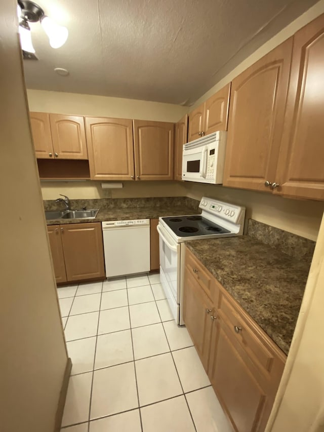 kitchen featuring white appliances, a sink, light tile patterned flooring, dark countertops, and a textured ceiling