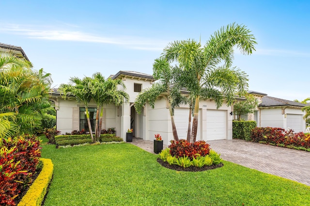 view of front facade featuring a front yard, stucco siding, an attached garage, and decorative driveway