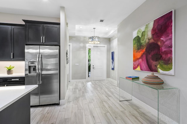 kitchen with stainless steel fridge, a tray ceiling, dark cabinets, light wood-style flooring, and light countertops