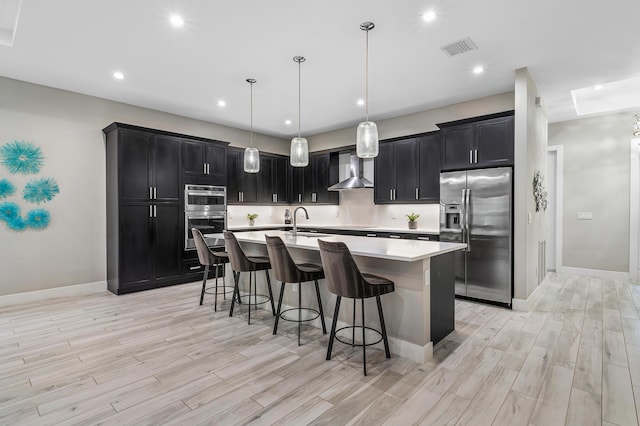 kitchen with dark cabinets, wall chimney range hood, visible vents, and appliances with stainless steel finishes