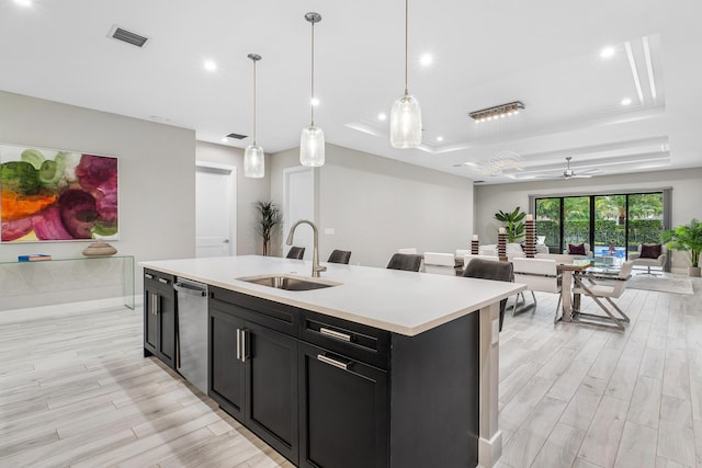 kitchen with a tray ceiling, dishwasher, dark cabinetry, a sink, and open floor plan