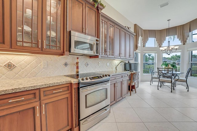 kitchen with glass insert cabinets, brown cabinets, stainless steel appliances, visible vents, and a chandelier