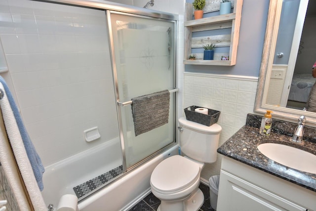 bathroom with tile walls, toilet, vanity, bath / shower combo with glass door, and wainscoting