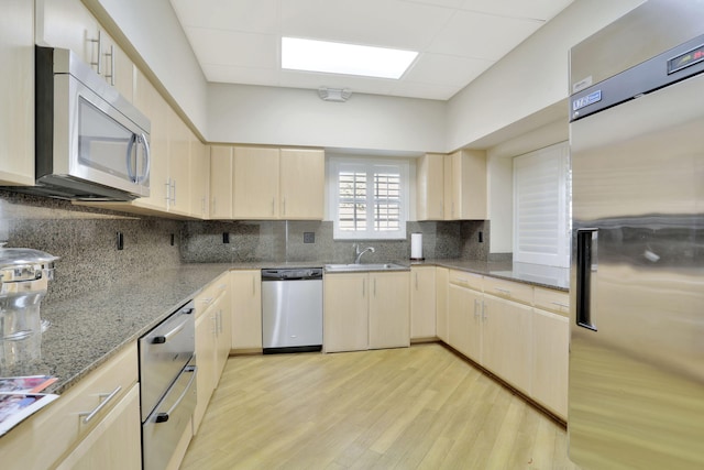 kitchen with light brown cabinetry, a sink, light wood-style floors, a paneled ceiling, and stainless steel appliances