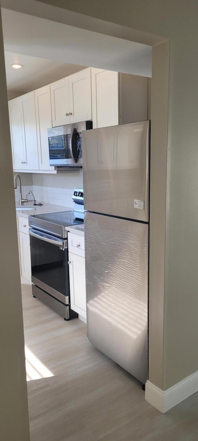 kitchen featuring white cabinets, stainless steel appliances, a sink, and light wood finished floors